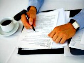 Man with cup of coffee going over paperwork with pen in right hand
