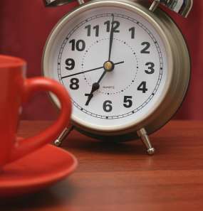 Alarm clock next to a red cup and saucer 