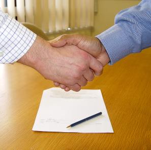 Two men shaking hands over pen and paper 