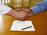 Two hands shaking in agreement over signed contract